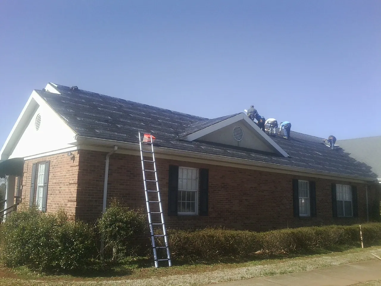 Crew tearing shingles off a brick ranch roof with a ladder set — Metal Roof Repair work by our crew in Foresthill