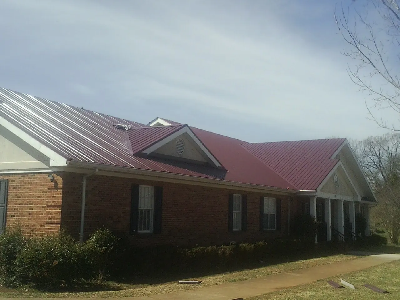 Red metal roof with gabled entries on a long brick building, from a Hail Damage Roof Repair job in Foresthill