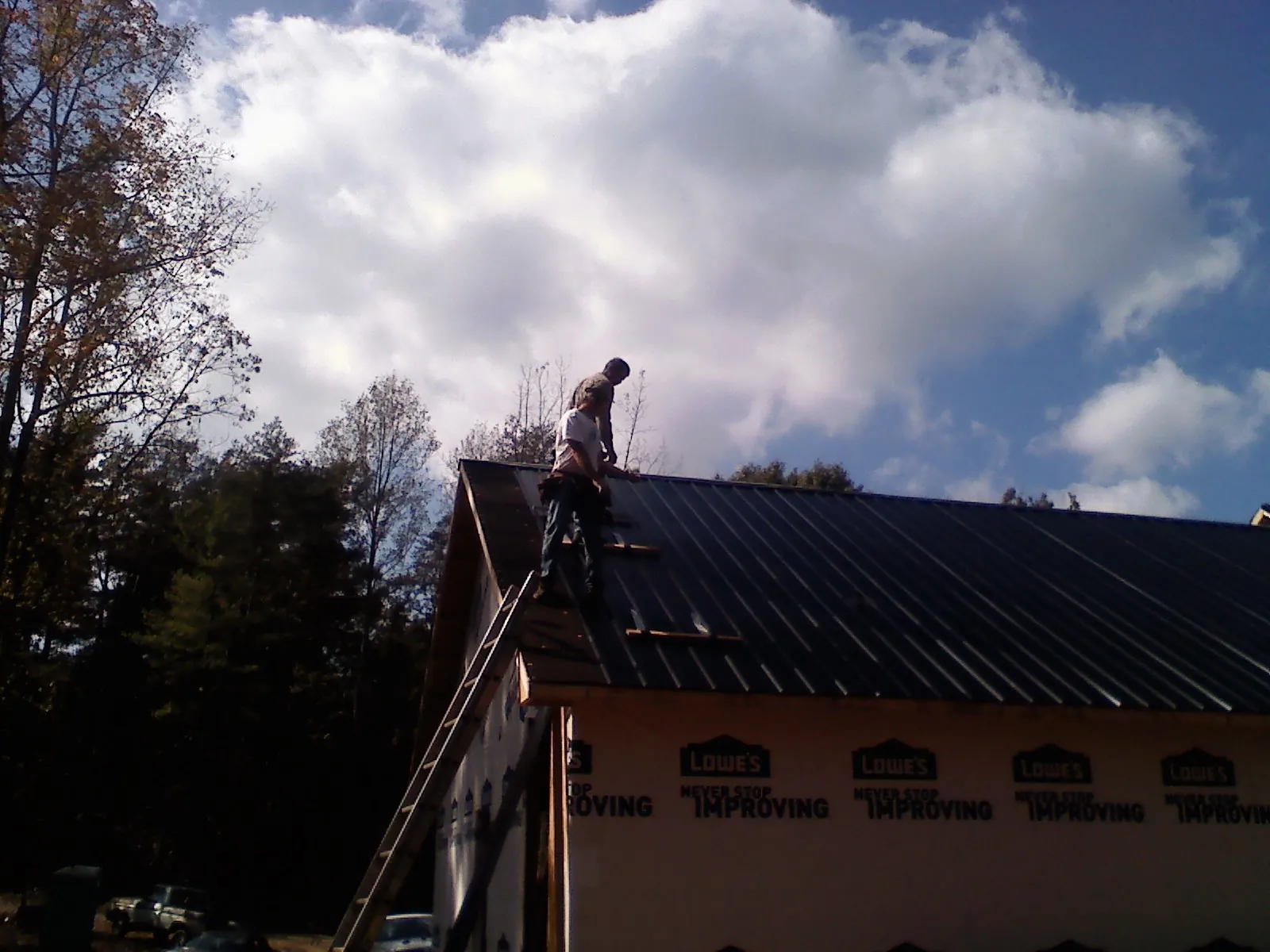 Roofer fastening dark metal panels high against a cloudy sky, from a Roof Inspection job in Foresthill